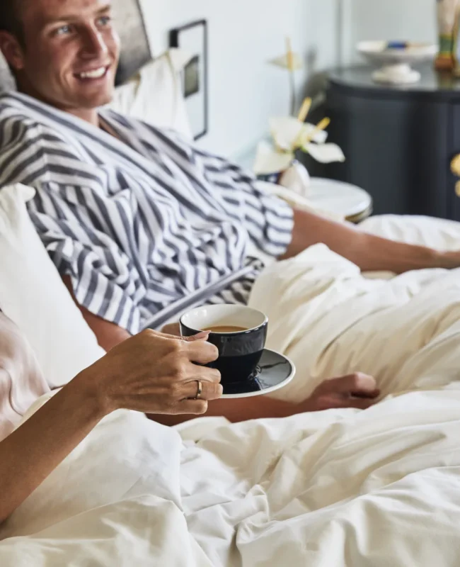 Happy couple lying in bed drinking coffee