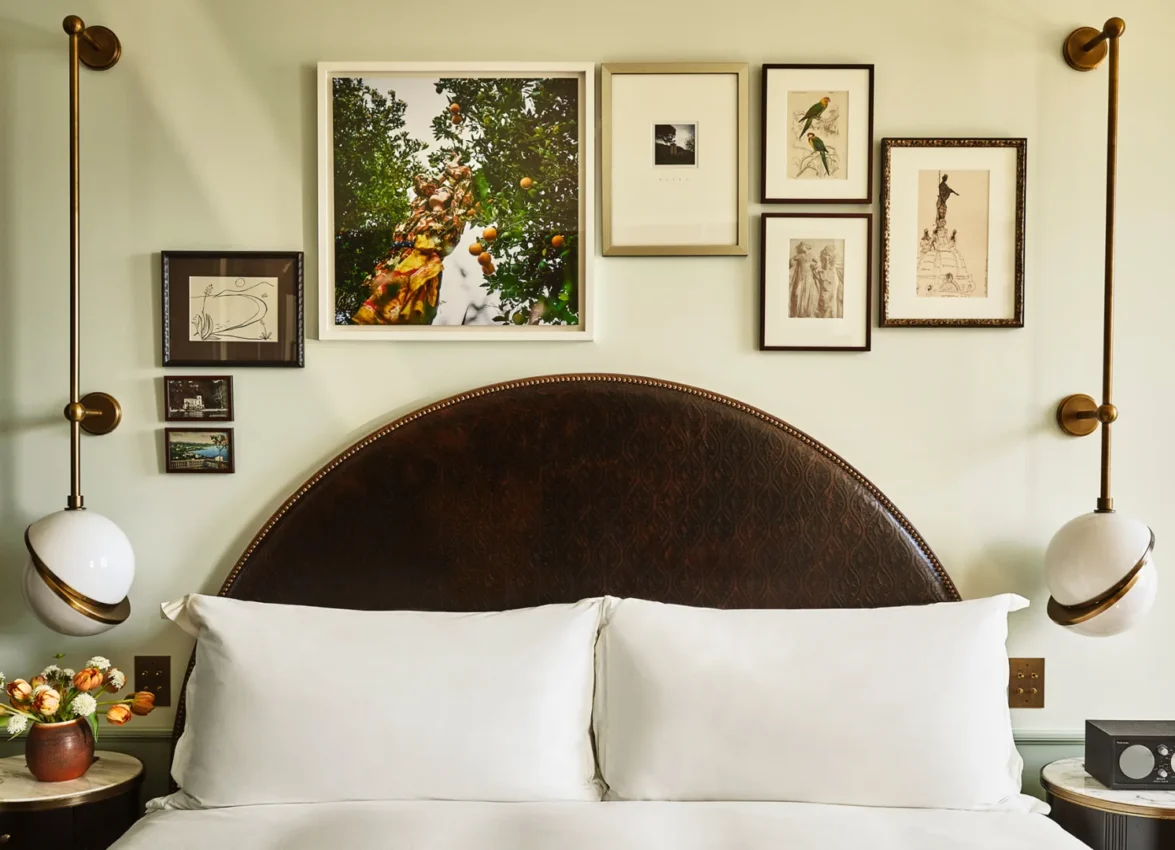 A collection of framed art hangs above twin beds with dark arched headboards in a boutique hotel room in LA.