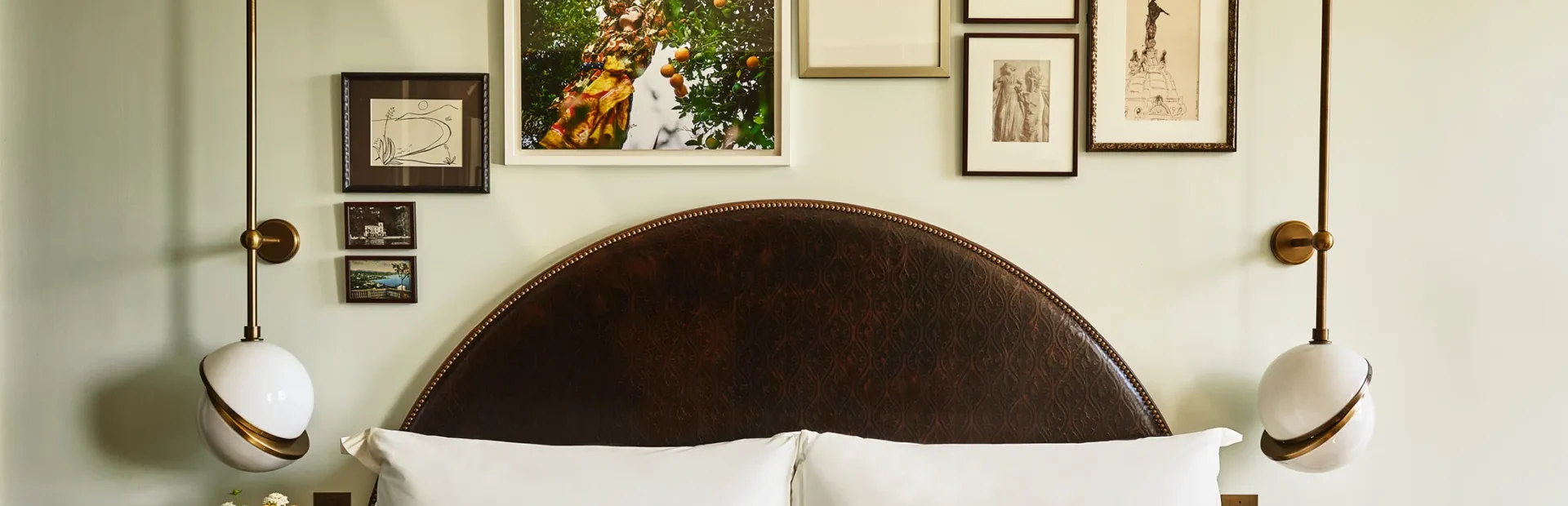 A collection of framed art hangs above twin beds with dark arched headboards in a boutique hotel room in LA.