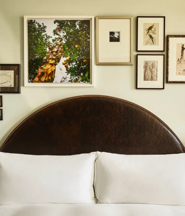 A collection of framed art hangs above twin beds with dark arched headboards in a boutique hotel room in LA.
