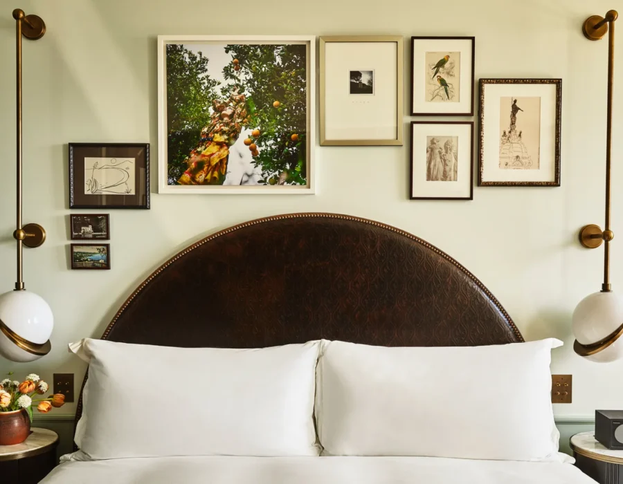 A collection of framed art hangs above twin beds with dark arched headboards in a boutique hotel room in LA.