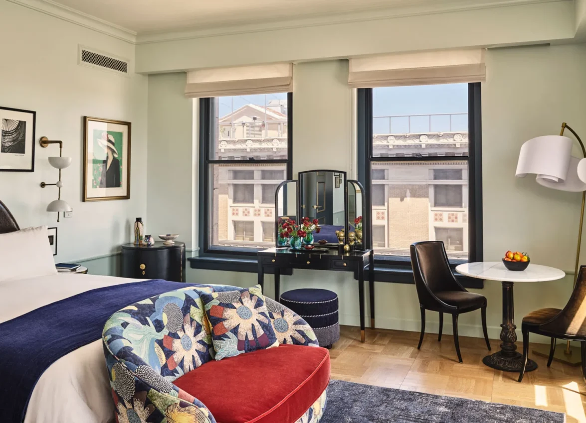 Art-filled guest room at Hotel Per La featuring plush white bedding and large windows overlooking downtown LA.