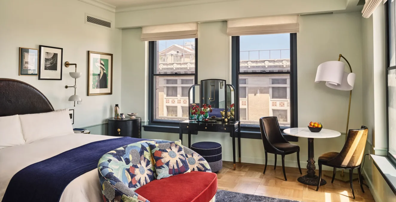 Art-filled guest room at Hotel Per La featuring plush white bedding and large windows overlooking downtown LA.
