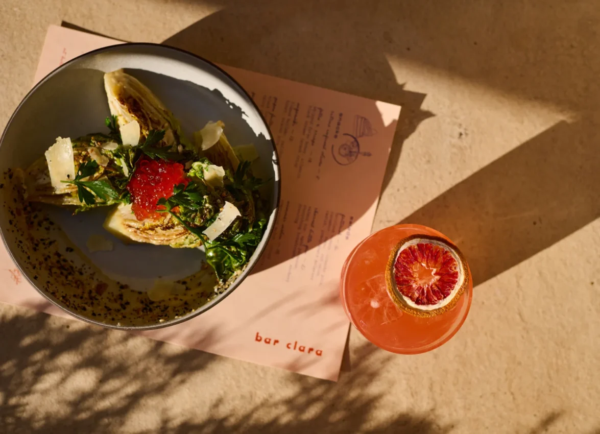 A refreshing cocktail and salad served on a sunlit table at Bar Clara, a premier rooftop bar in Los Angeles, CA.