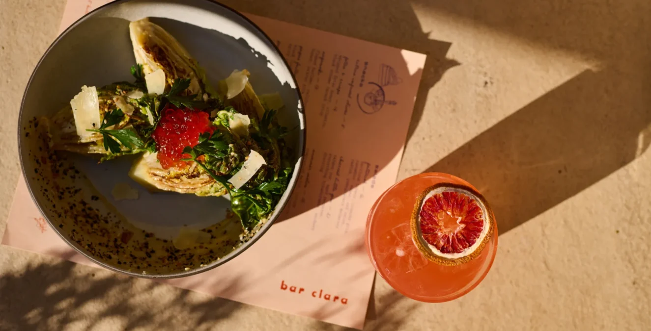 A refreshing cocktail and salad served on a sunlit table at Bar Clara, a premier rooftop bar in Los Angeles, CA.