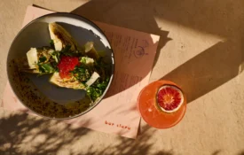 A refreshing cocktail and salad served on a sunlit table at Bar Clara, a premier rooftop bar in Los Angeles, CA.
