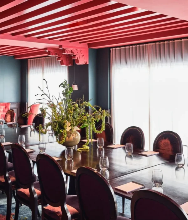 Velvet chairs surround a long conference table in a sophisticated Hotel Per La event space with pink rafter ceilings.