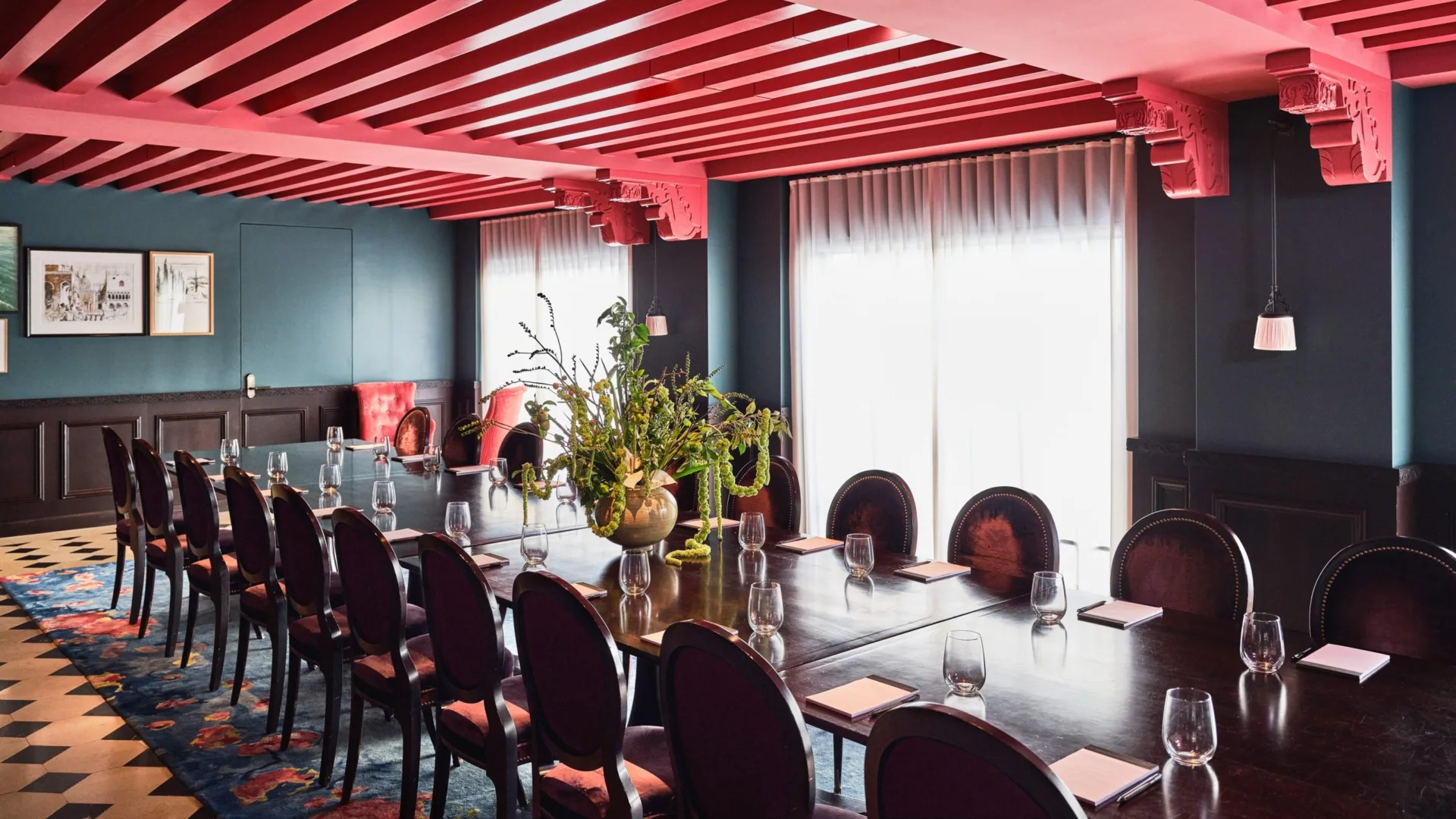 Velvet chairs surround a long conference table in a sophisticated Hotel Per La event space with pink rafter ceilings.