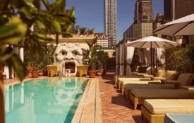 Sun loungers line a bright blue rooftop pool at Bar Clara with a sculpted stone face and city skyline views.