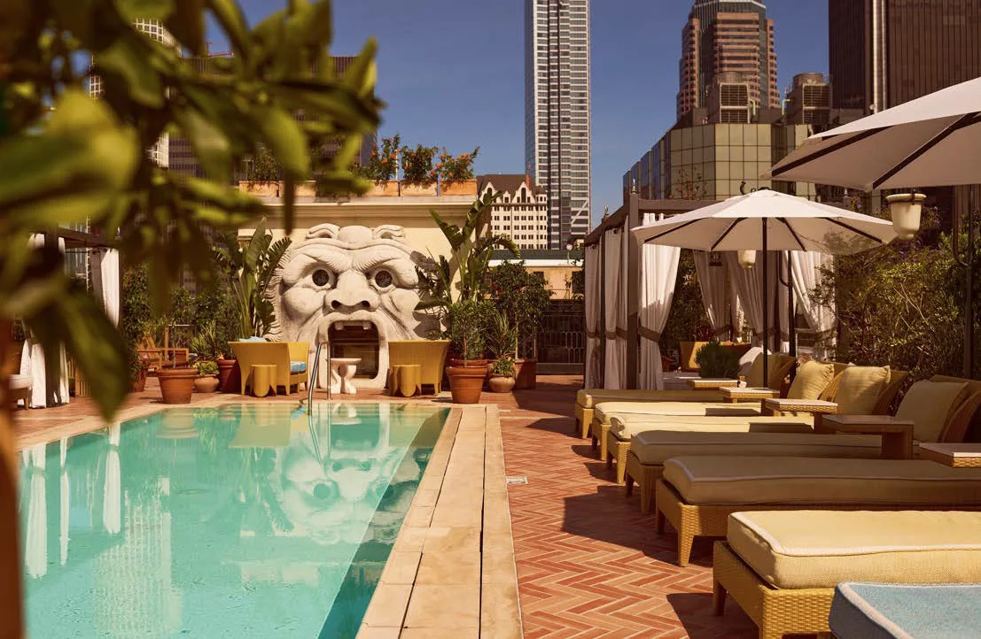 Sun loungers line a bright blue rooftop pool at Bar Clara with a sculpted stone face and city skyline views.