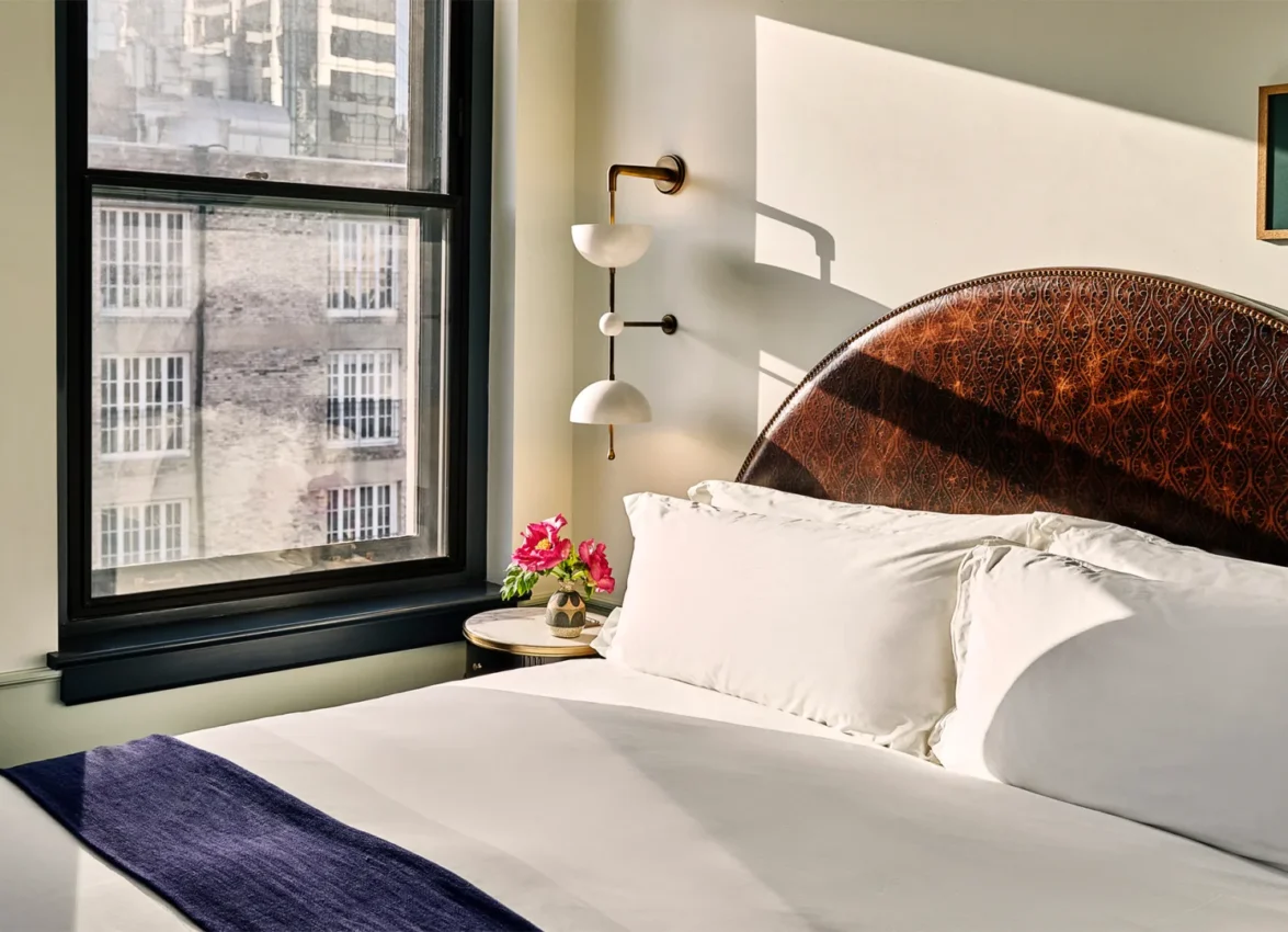 A sun-drenched hotel room at Hotel Per La features a detailed leather headboard and views of downtown Los Angeles.