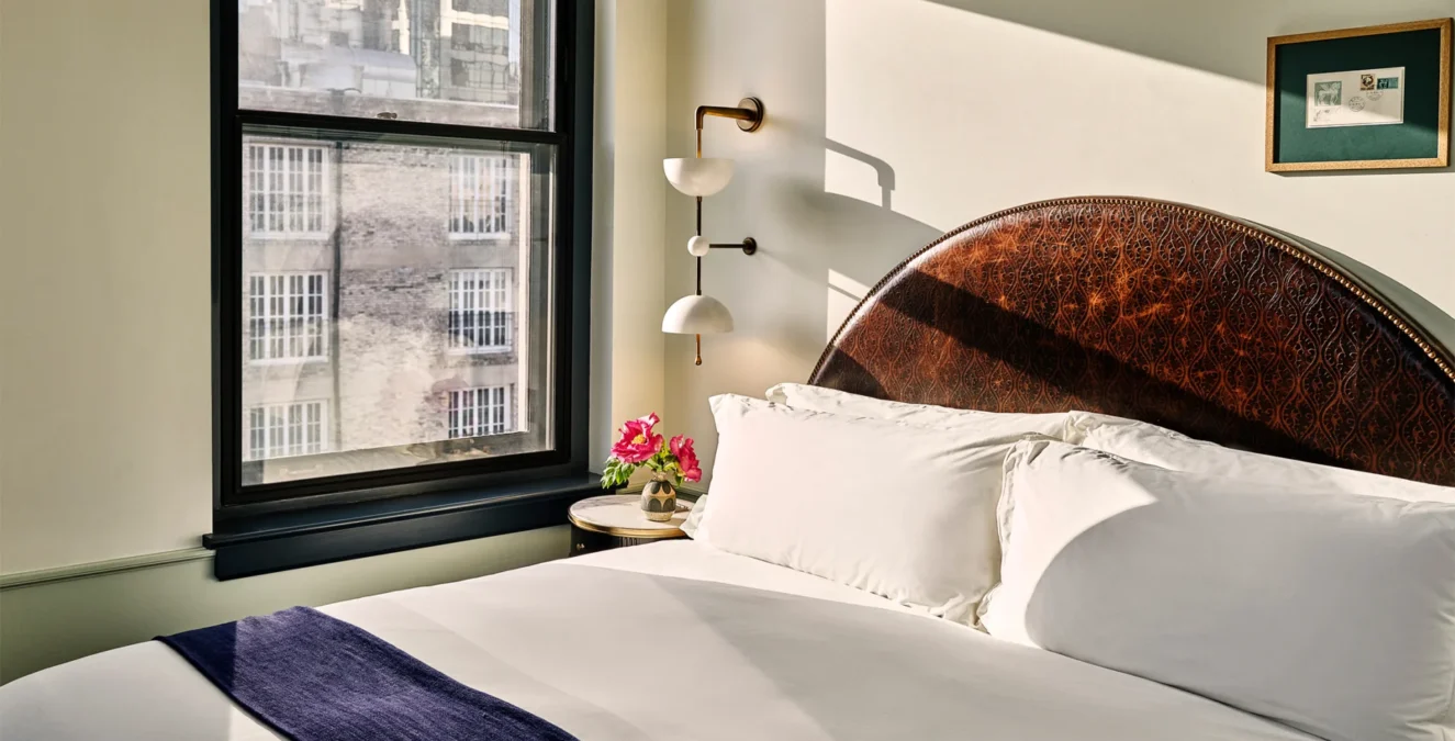 A sun-drenched hotel room at Hotel Per La features a detailed leather headboard and views of downtown Los Angeles.