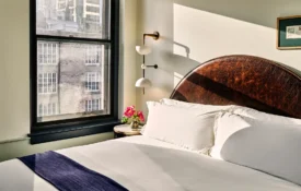 A sun-drenched hotel room at Hotel Per La features a detailed leather headboard and views of downtown Los Angeles.