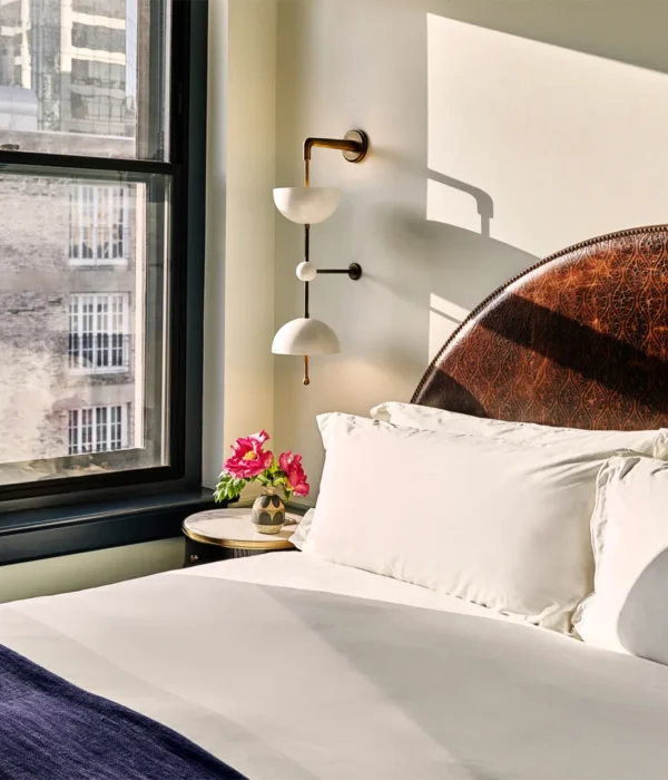 A sun-drenched hotel room at Hotel Per La features a detailed leather headboard and views of downtown Los Angeles.