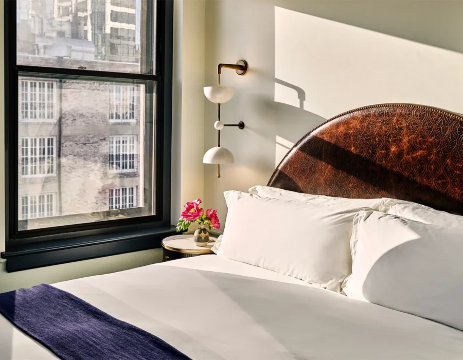 A sun-drenched hotel room at Hotel Per La features a detailed leather headboard and views of downtown Los Angeles.