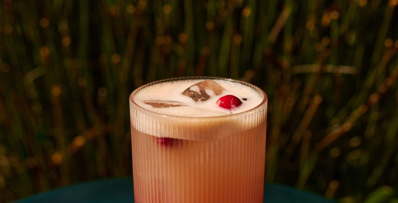 A layered pink and peach cocktail with a cranberry garnish at Bar Clara, a premier rooftop bar in Los Angeles.