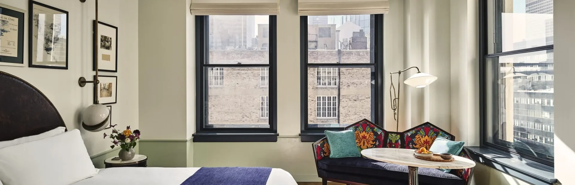 A stylish hotel room featuring a patterned settee, large windows, and plush bedding at Hotel Per La in Los Angeles.