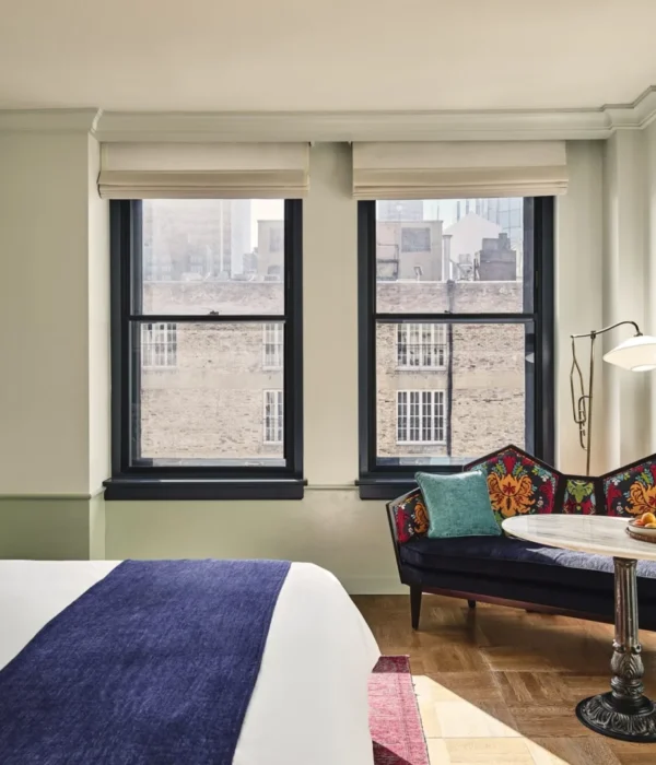 A stylish hotel room featuring a patterned settee, large windows, and plush bedding at Hotel Per La in Los Angeles.