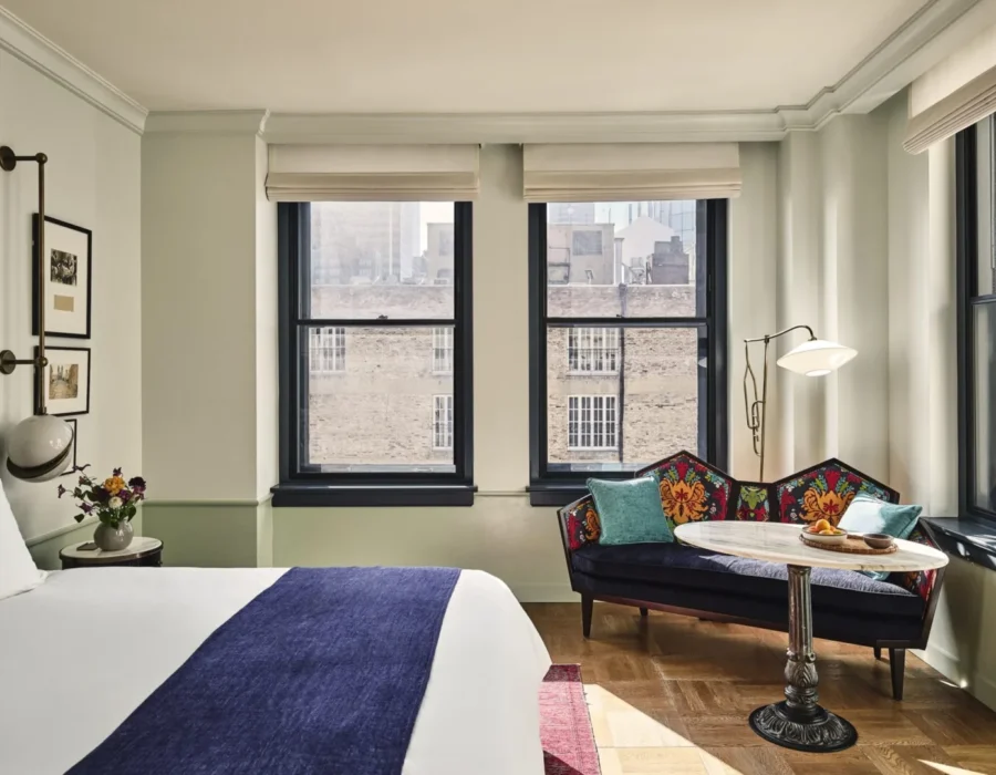 A stylish hotel room featuring a patterned settee, large windows, and plush bedding at Hotel Per La in Los Angeles.