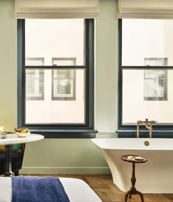 A white freestanding soaking tub sits beneath large windows in a luxury boutique hotel suite in Los Angeles.