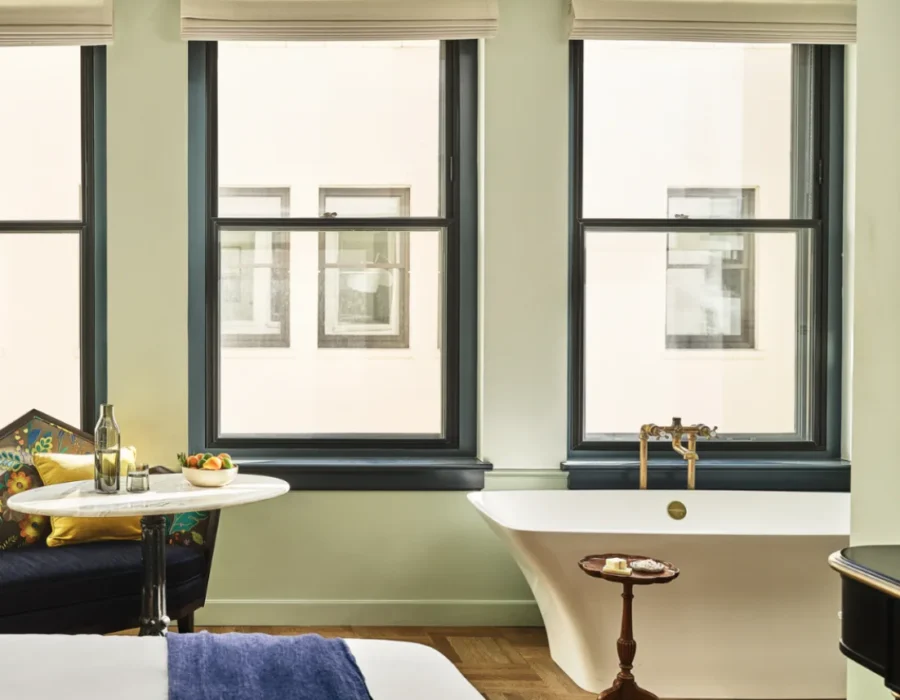 A white freestanding soaking tub sits beneath large windows in a luxury boutique hotel suite in Los Angeles.