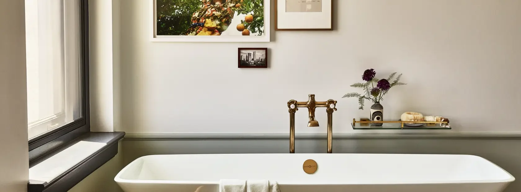 A sleek white soaking tub with vintage brass fixtures and curated art defines this luxury Los Angeles hotel suite.