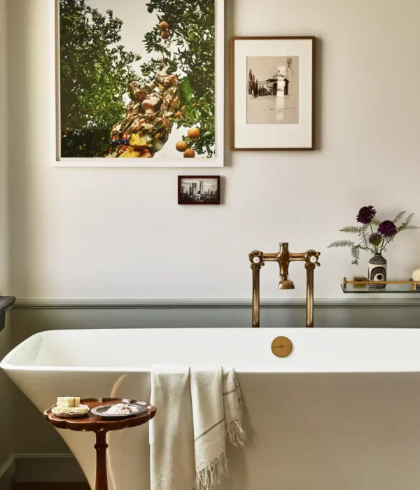 A sleek white soaking tub with vintage brass fixtures and curated art defines this luxury Los Angeles hotel suite.