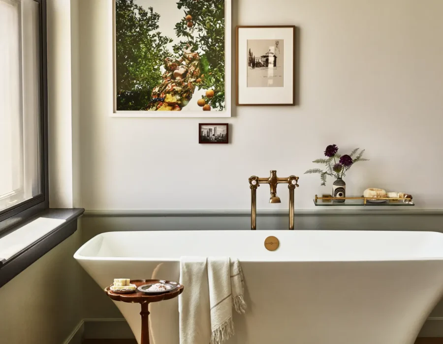 A sleek white soaking tub with vintage brass fixtures and curated art defines this luxury Los Angeles hotel suite.
