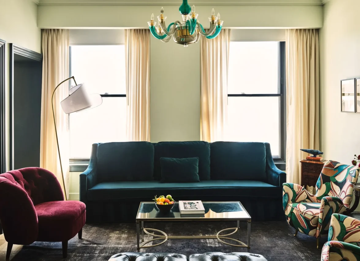 An elegant living room in a Los Angeles suite featuring a velvet teal sofa, patterned chairs, and a green chandelier.