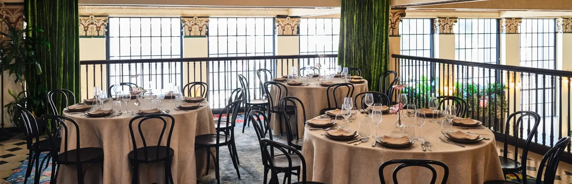 Formal round tables set for a banquet in an elegant Los Angeles event space with ornate columns and velvet curtains.