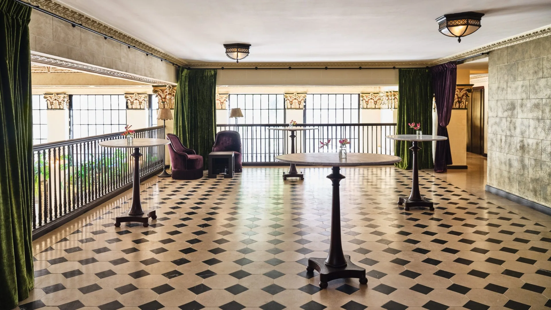 A mezzanine event space features checkered flooring, tall cocktail tables, and rich velvet drapes in Los Angeles.
