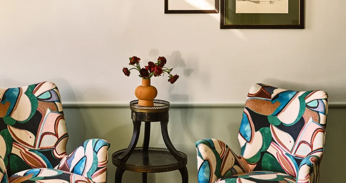 Two vibrant patterned armchairs flank a side table with fresh flowers in a luxury Los Angeles hotel suite.