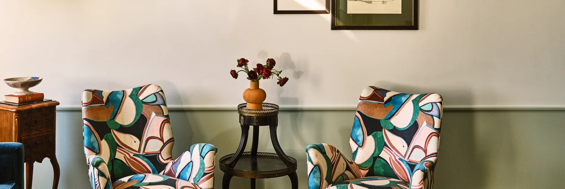 Two vibrant patterned armchairs flank a side table with fresh flowers in a luxury Los Angeles hotel suite.