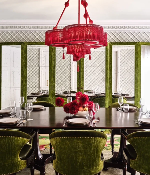 A grand dark wood table and green velvet chairs sit beneath a red chandelier at Ristorante Per L'Ora in Los Angeles.
