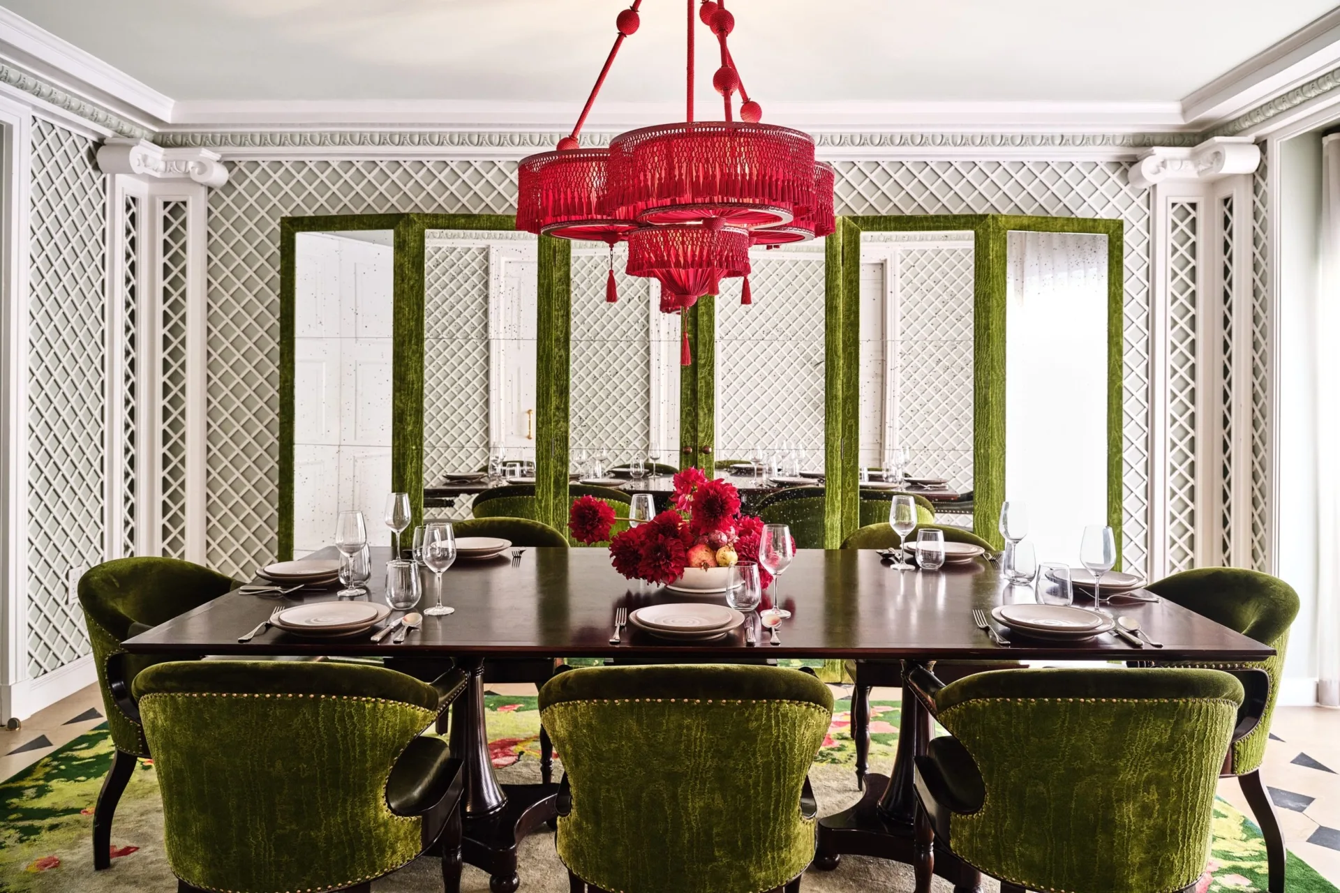 A grand dark wood table and green velvet chairs sit beneath a red chandelier at Ristorante Per L'Ora in Los Angeles.