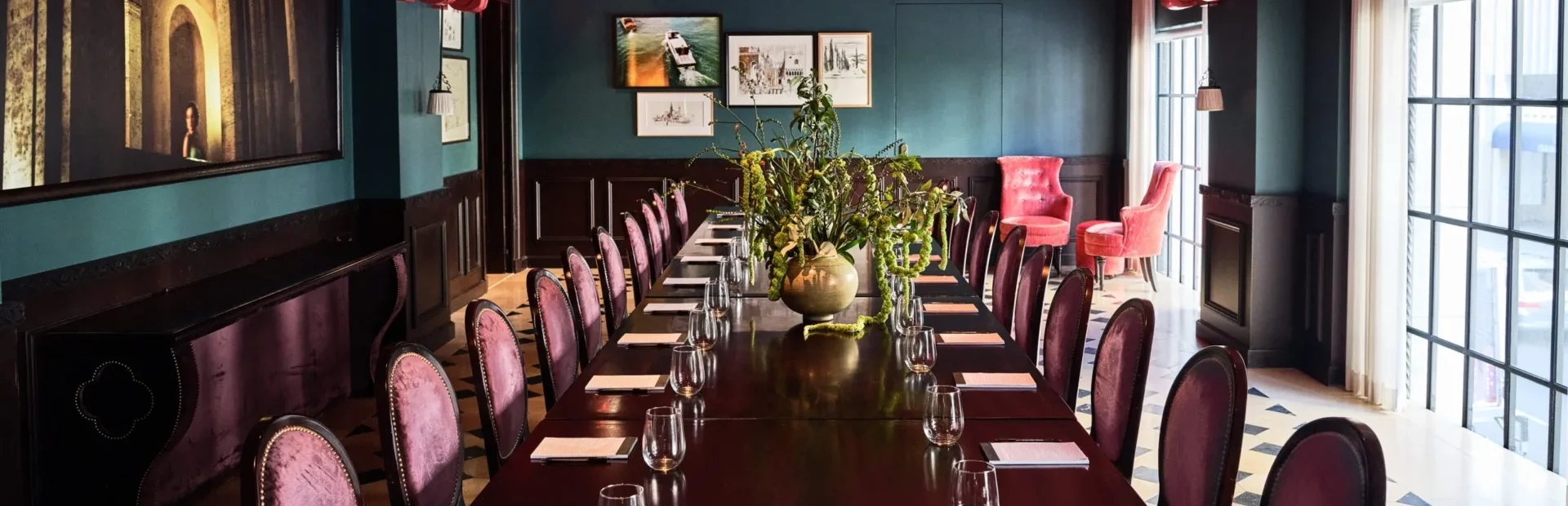 Velvet chairs surround a long dark wood table in a luxury Los Angeles event space with a red beamed ceiling.