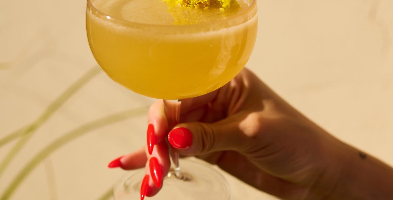 A yellow floral cocktail held against a sunny wall at Bar Clara, a top rooftop bar in Los Angeles, CA.