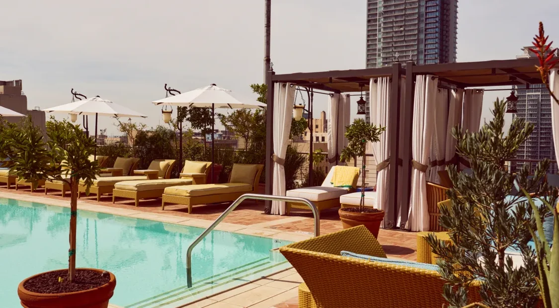 A serene rooftop pool at Hotel Per La features white umbrellas, plush loungers, and private cabanas in Los Angeles.