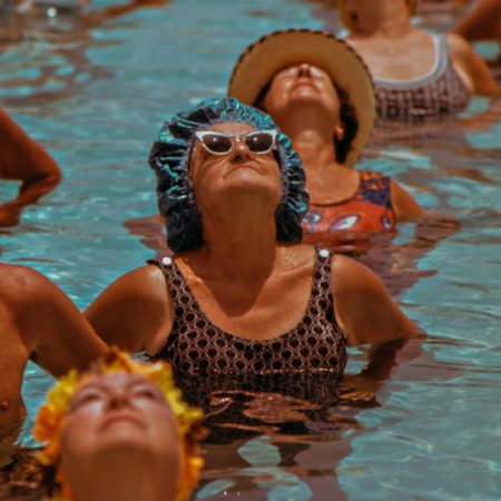 A group of women in vintage swim caps look up towards the sun in the rooftop pool at Hotel Per La.
