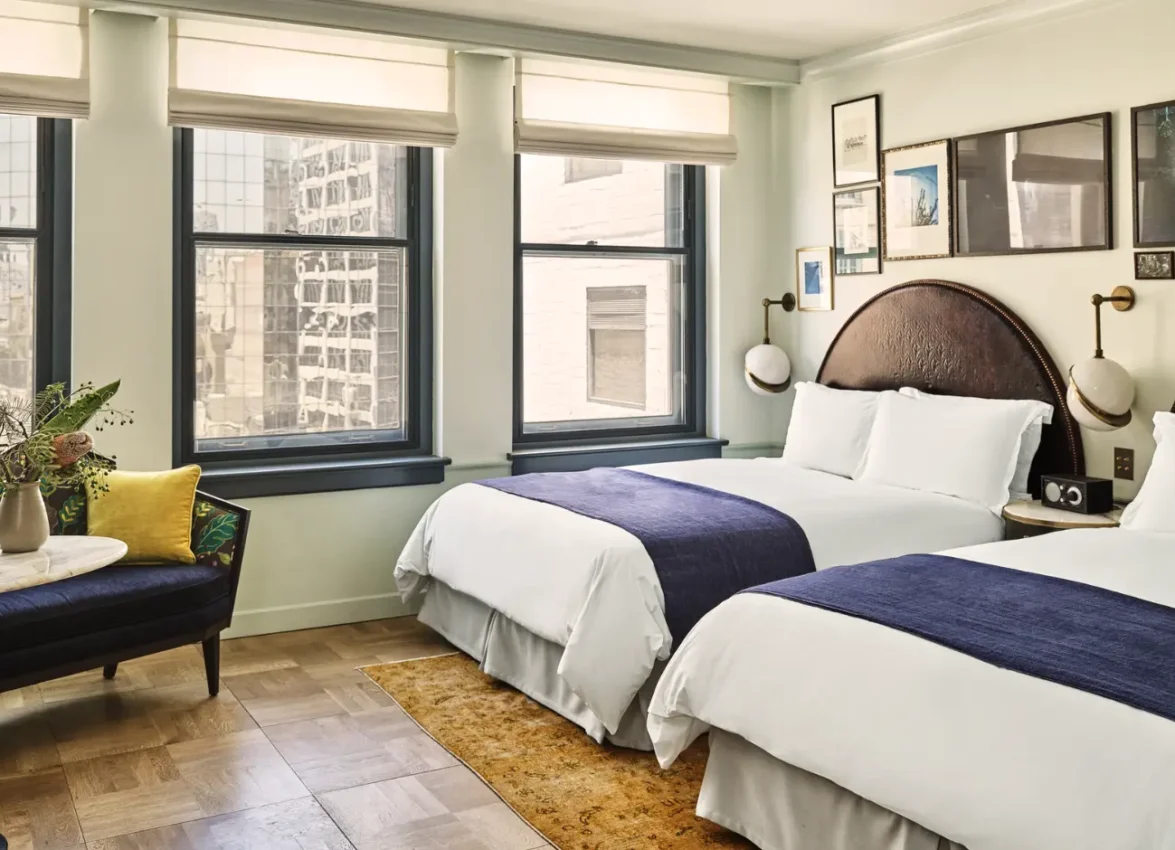 A hotel room with two large beds and a couch with a marble side table.