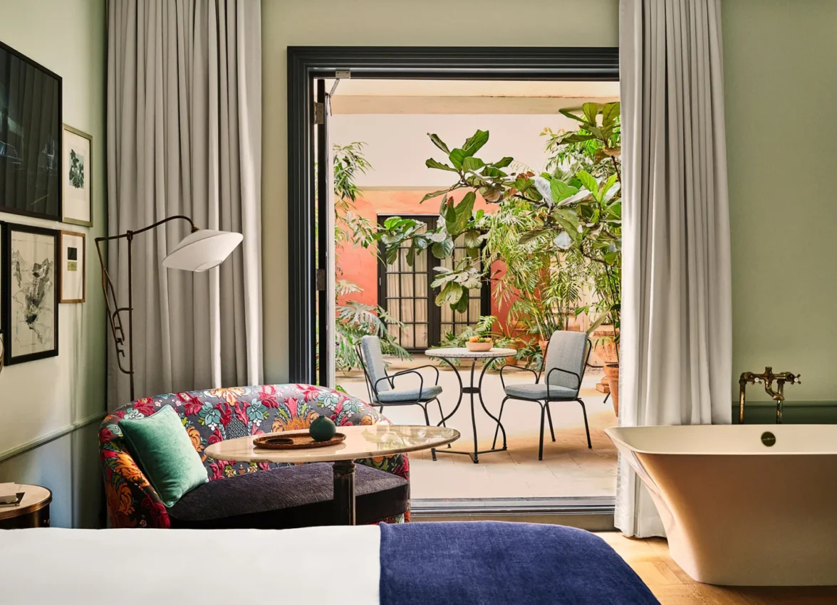 A bright hotel suite at Hotel Per La with a floral loveseat, soaking tub, and a lush private outdoor courtyard.