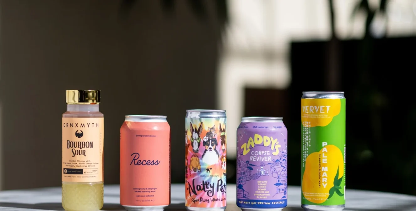 A colorful lineup of craft canned cocktails and bottled drinks on a marble counter at Bar Clara in Los Angeles.