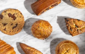 An assortment of golden-brown artisan pastries and fresh bread from Cafe Ora displayed on a white marble surface.
