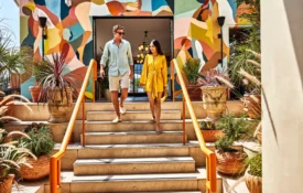 A couple walks down stone steps past vibrant murals and lush greenery at the Bar Clara rooftop bar in Los Angeles.