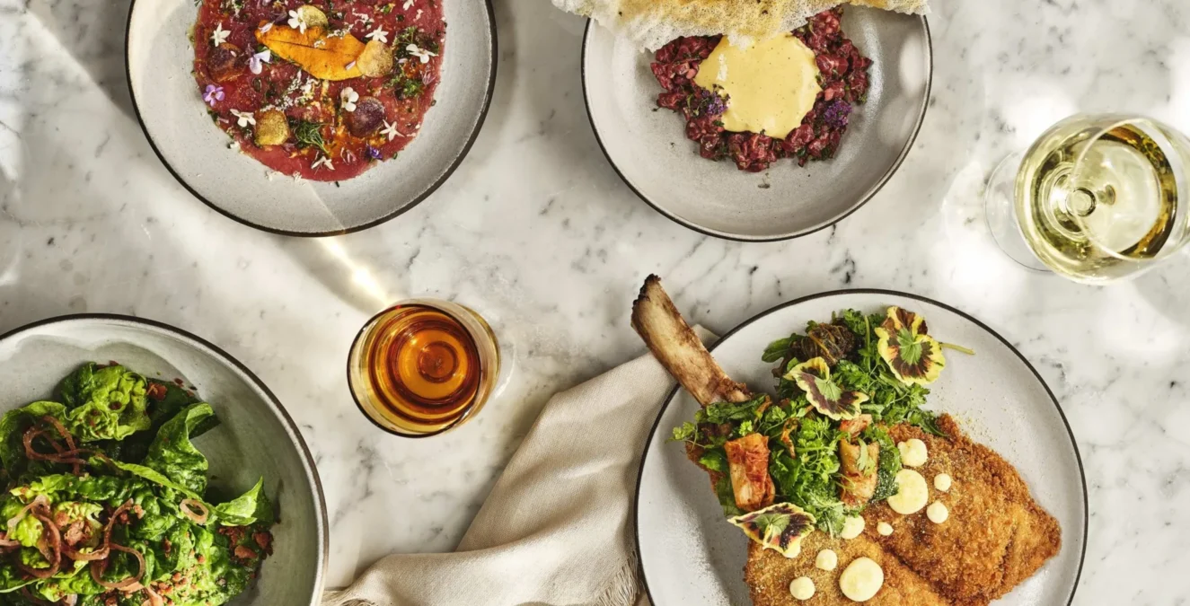 A marble table spread with gourmet Italian dishes including veal milanese and beef tartare at Ristorante Per L'Ora.
