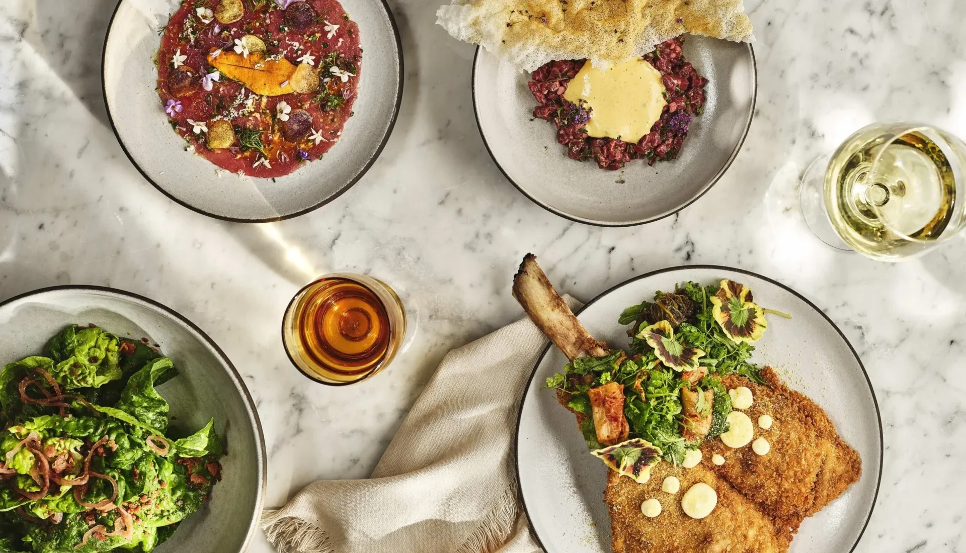 A marble table spread with gourmet Italian dishes including veal milanese and beef tartare at Ristorante Per L'Ora.