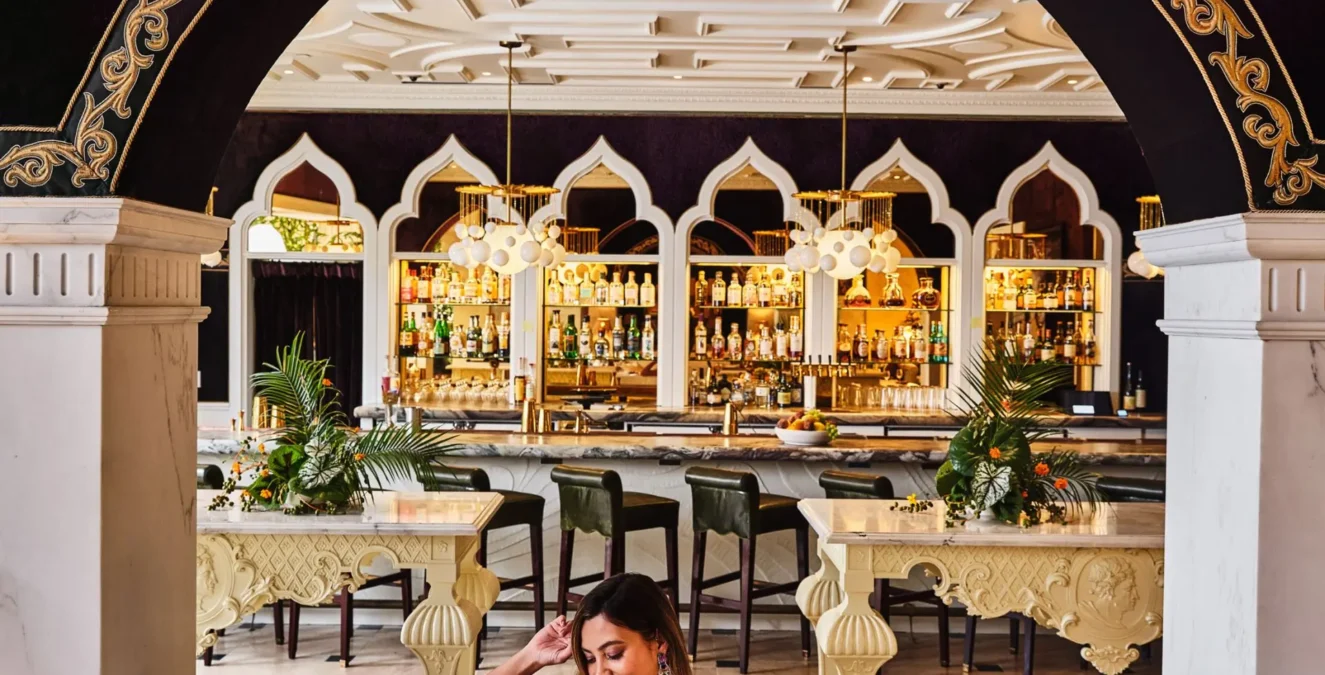 A woman enjoys a drink on a white sofa in the ornate, arched lounge area of our boutique hotel in Los Angeles.