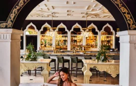 A woman enjoys a drink on a white sofa in the ornate, arched lounge area of our boutique hotel in Los Angeles.
