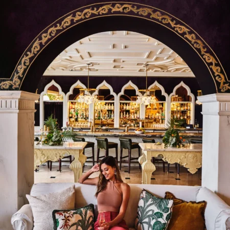 A woman enjoys a drink on a white sofa in the ornate, arched lounge area of our boutique hotel in Los Angeles.