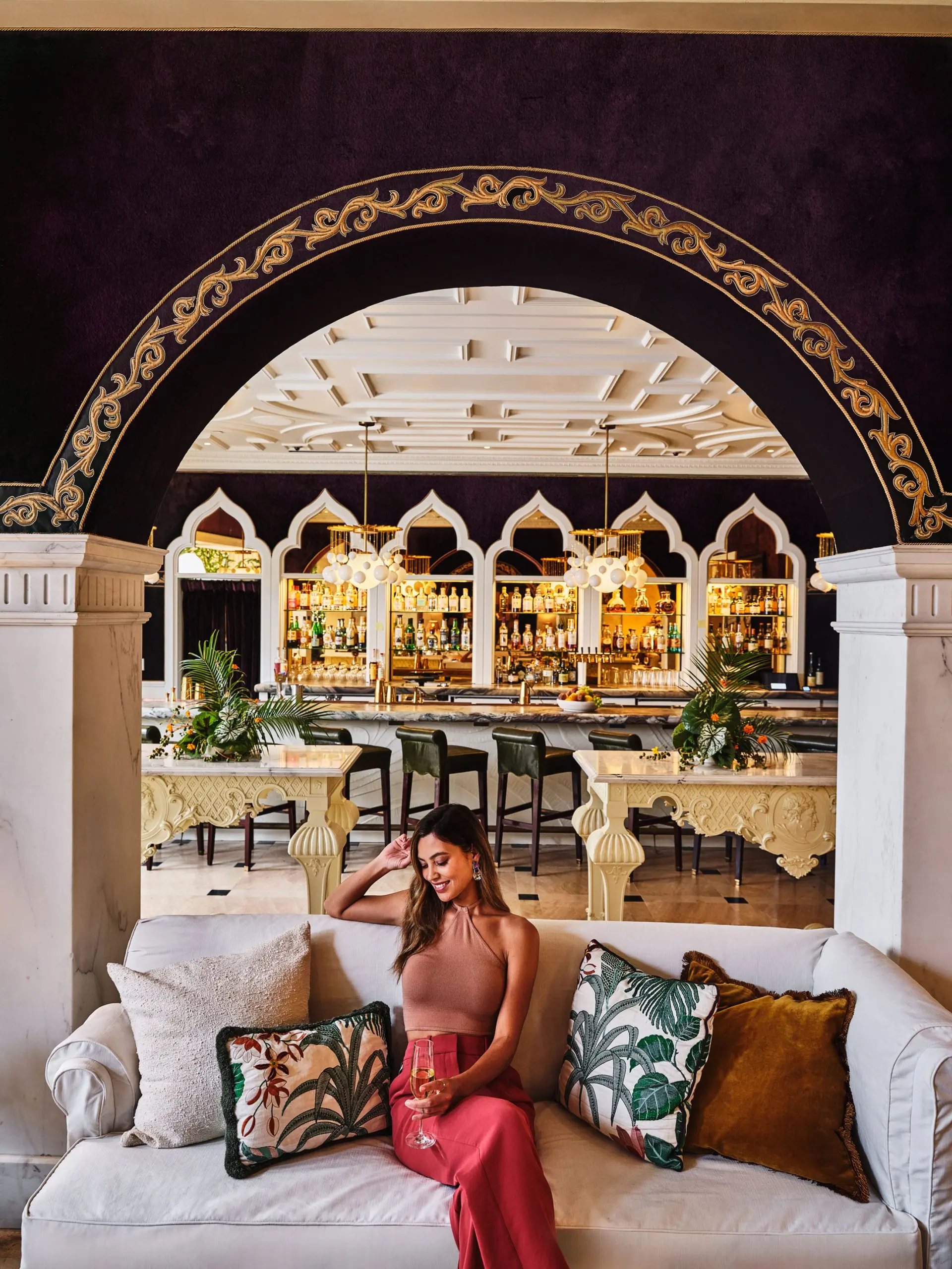 A woman enjoys a drink on a white sofa in the ornate, arched lounge area of our boutique hotel in Los Angeles.